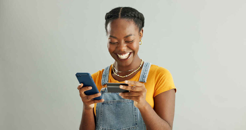 Young woman looking at her debit card and holding her mobile phone